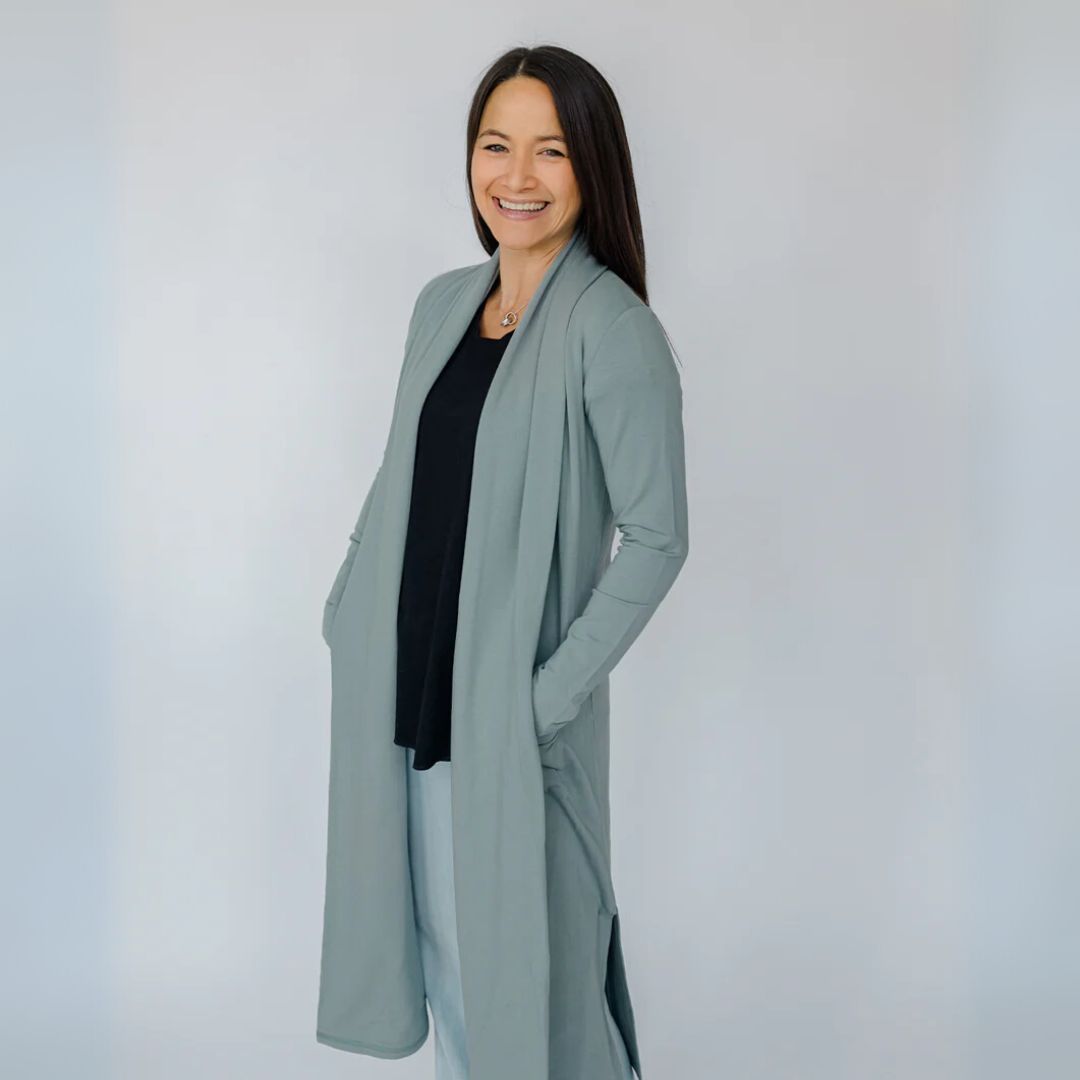 Woman wearing a long light blue coat over a black top against a white background