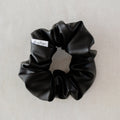 Black scrunchie with a brand label on a light gray background