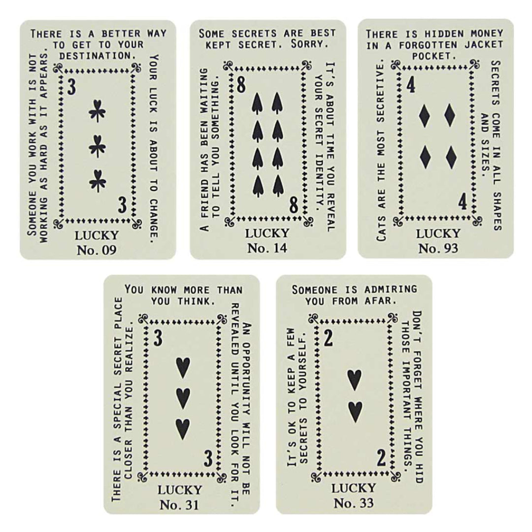 A greeting card with a dark grey background and a decorative white border at the top. The text "PICK A CARD" is at the top, followed by "BRIGHTEN UP YOUR DAY, AN UNEXPECTED SECRET REVEALED." Below the text are five fan-arranged cards with a yellow and white patterned back, held by a paperclip. A second image shows five individual fortune cards, each resembling a playing card with suit symbols and text. The fortunes include messages like "YOUR LUCK IS ABOUT TO CHANGE," "ALL YOUR DREAMS WILL COME TRUE," and "