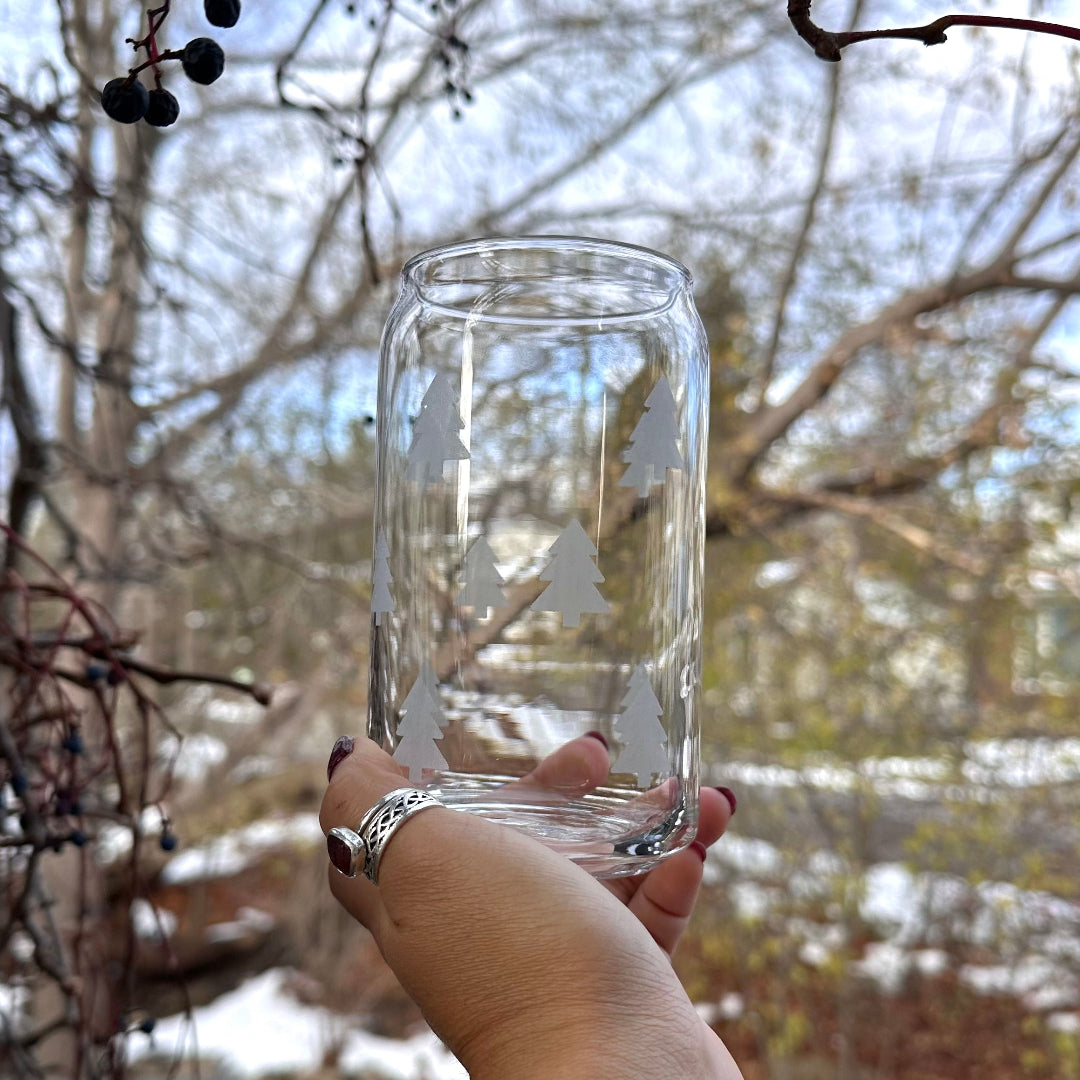 Clear glass with engraved design held in front of leafless trees and a building.