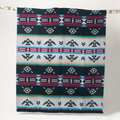 The Éclair Eco-Friendly Everyday Blanket by Mini Tipi, featuring bold Indigenous-inspired geometric patterns in black, grey, burgundy, turquoise, and yellow, hanging from a natural branch. This sustainable and stylish blanket is available in Ottawa, Ontario, Canada.