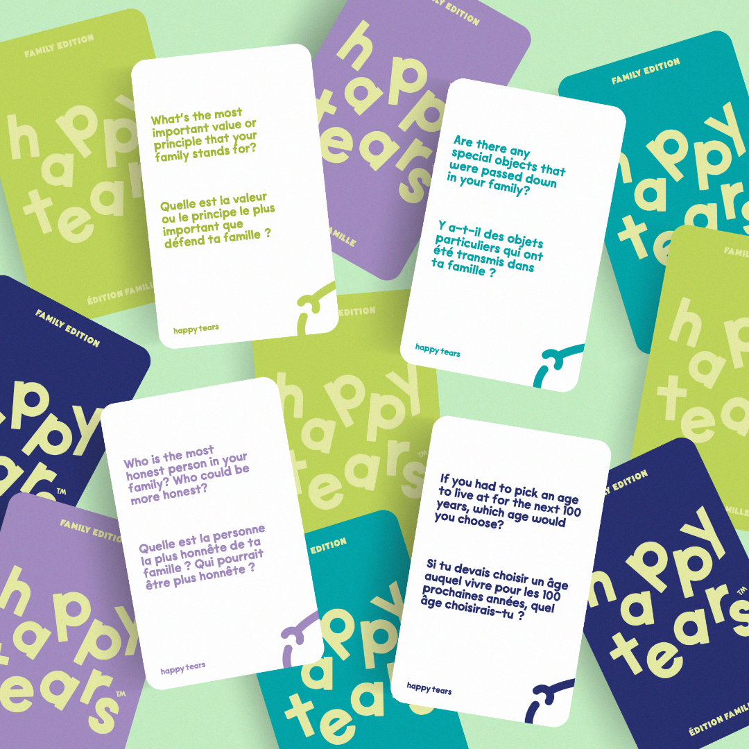 Happy Tears Family Edition deck, Ottawa. Grey linen pouch, rainbow-coloured cards. 'Happy Tears' logo, bilingual text: 'Family connection for all ages', 'Liens familiales pour tous les ages'. Local Ottawa board games.