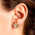 Gold flower-shaped earring with a central gemstone worn by a person.