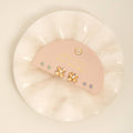 Pink earrings with gold accents in a clear plastic case on a light beige background