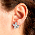 Silver flower-shaped earring with a pearl center worn by a person.