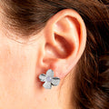 Silver flower-shaped earring worn on an ear with brown hair.