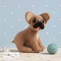 Small brown dog toy with a black nose on a light wooden surface against a light blue background with white polka dots.