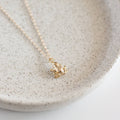 Gold frog pendant necklace on a light gray speckled ceramic plate