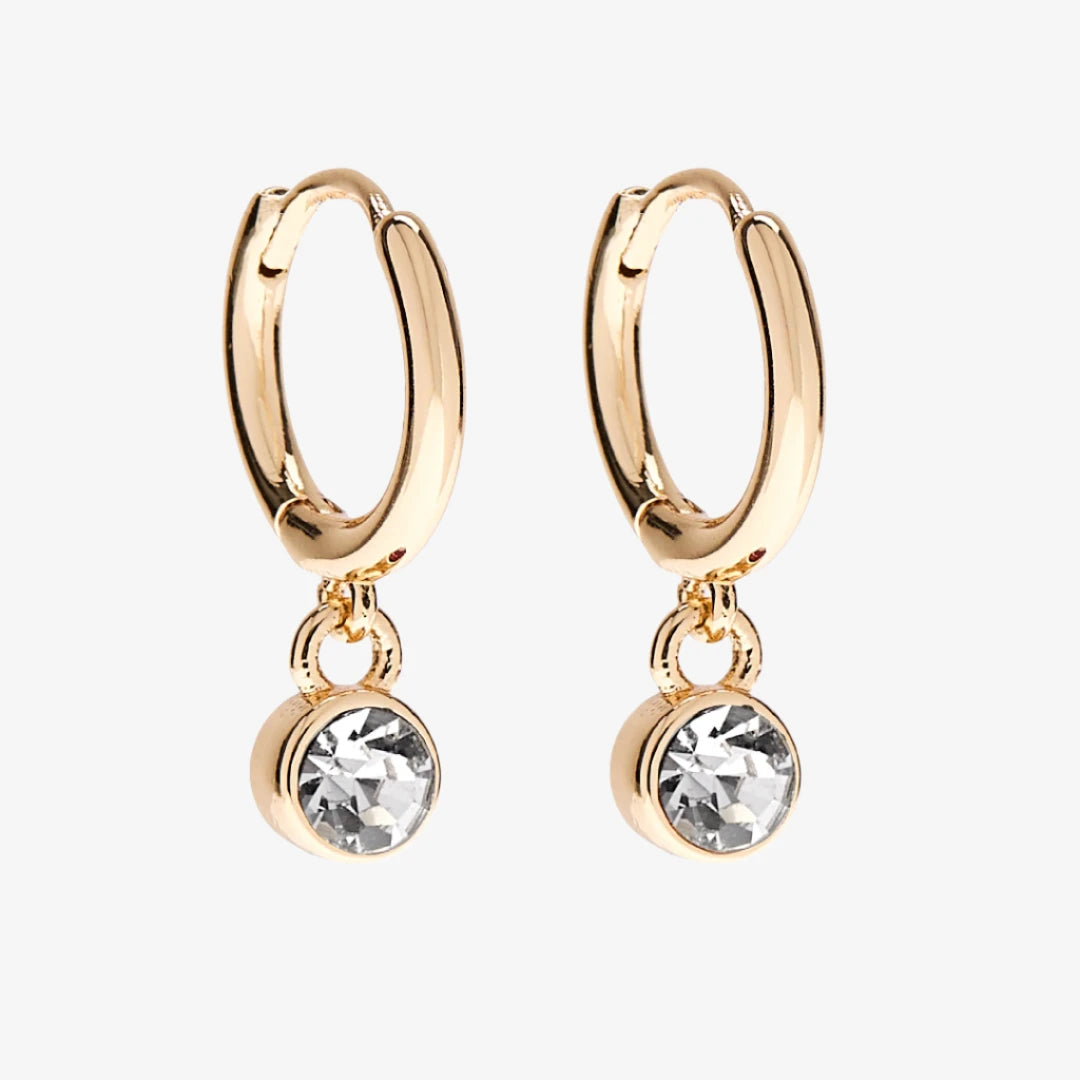 A set of three pairs of quartz earrings displayed on a pink card. The set includes a pair of stud earrings, a pair of bar earrings with small quartz beads, and a pair of hoop earrings with dangling quartz stones. The card has the month "April" and the brand name "Foxy Originals."