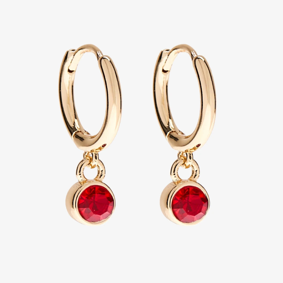 A set of three pairs of ruby earrings displayed on a red card. The set includes a pair of stud earrings, a pair of bar earrings with small ruby beads, and a pair of hoop earrings with dangling ruby stones. The card has the month "July" and the brand name "Foxy Originals."