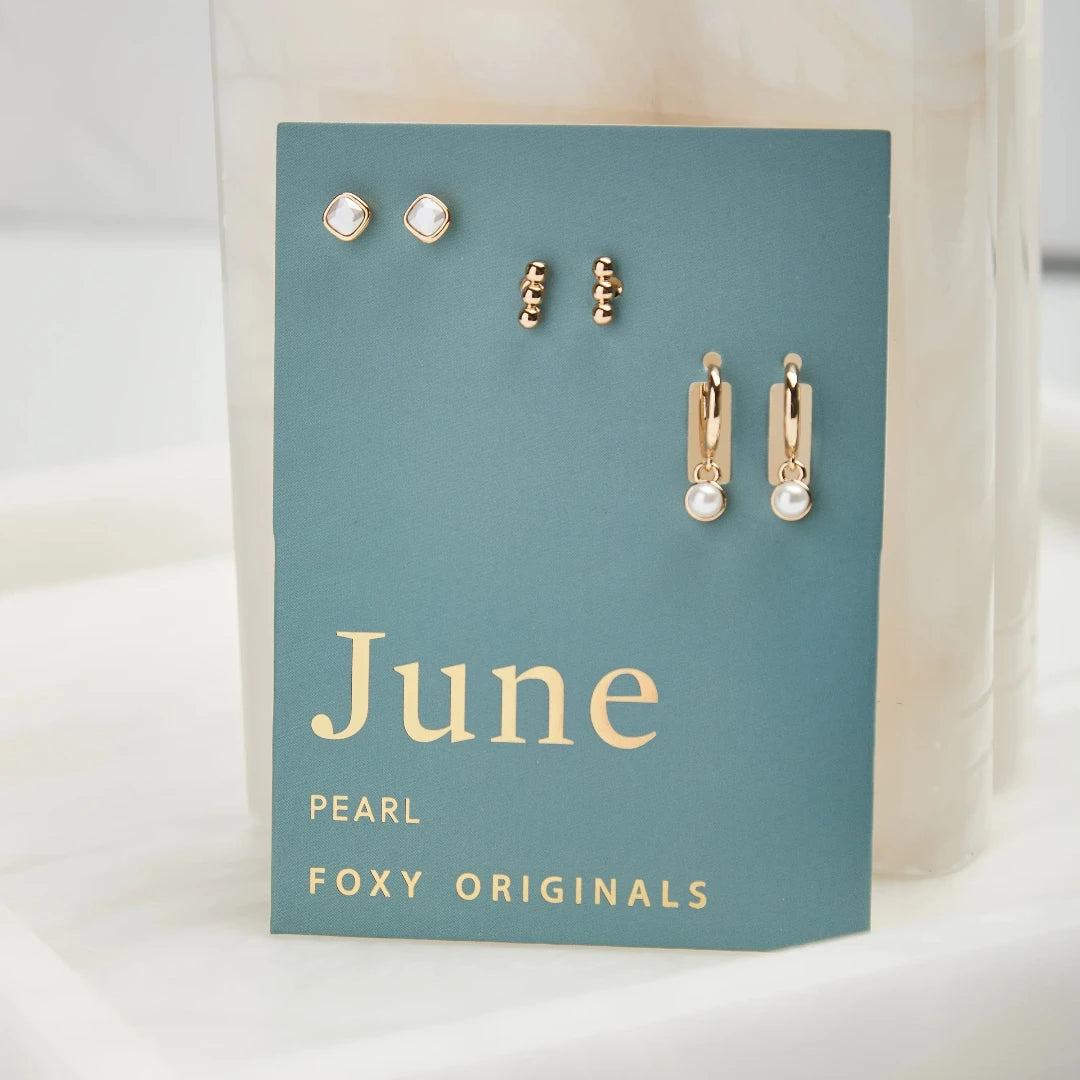 A set of three pairs of pearl earrings displayed on a blue card. The set includes a pair of stud earrings, a pair of bar earrings with small pearl beads, and a pair of hoop earrings with dangling pearl stones. The card has the month "June" and the brand name "Foxy Originals."
