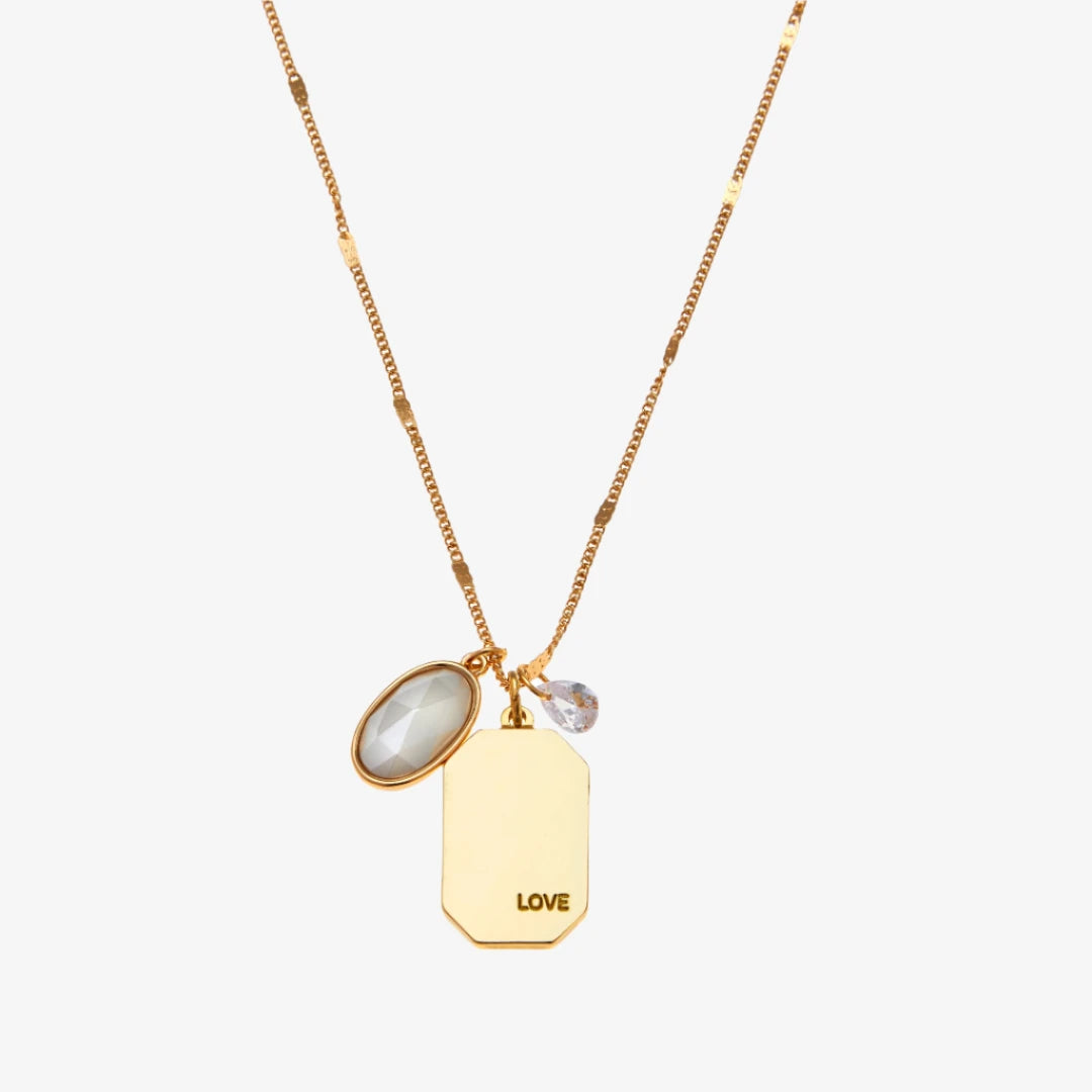 A gold necklace with a pearl stone pendant. The pendant also has the word "LOVE" engraved on it. The necklace is displayed on a blue card with the month "June" and the brand name "Foxy Originals."