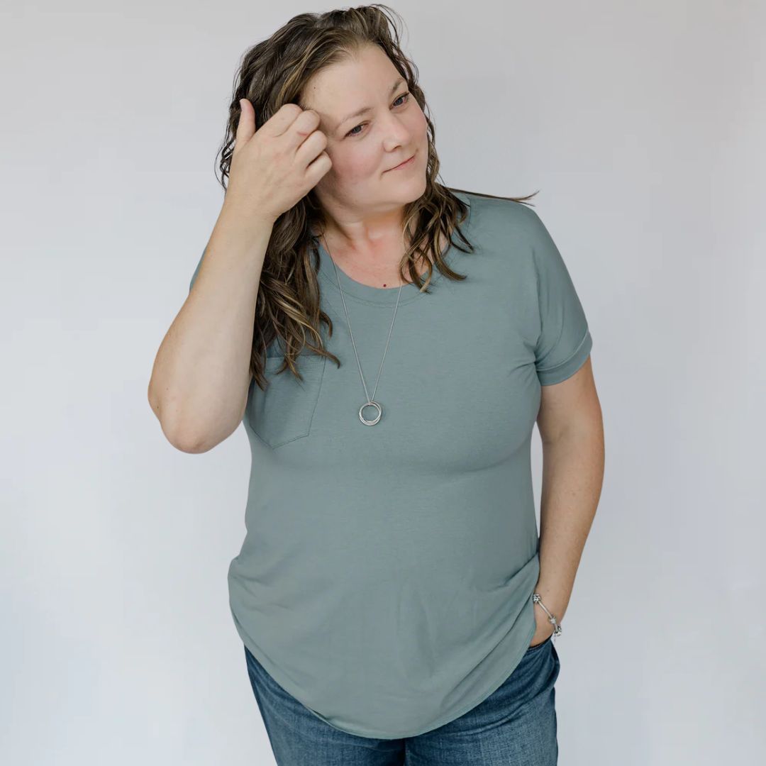 Woman wearing a green t-shirt and blue jeans against a plain background