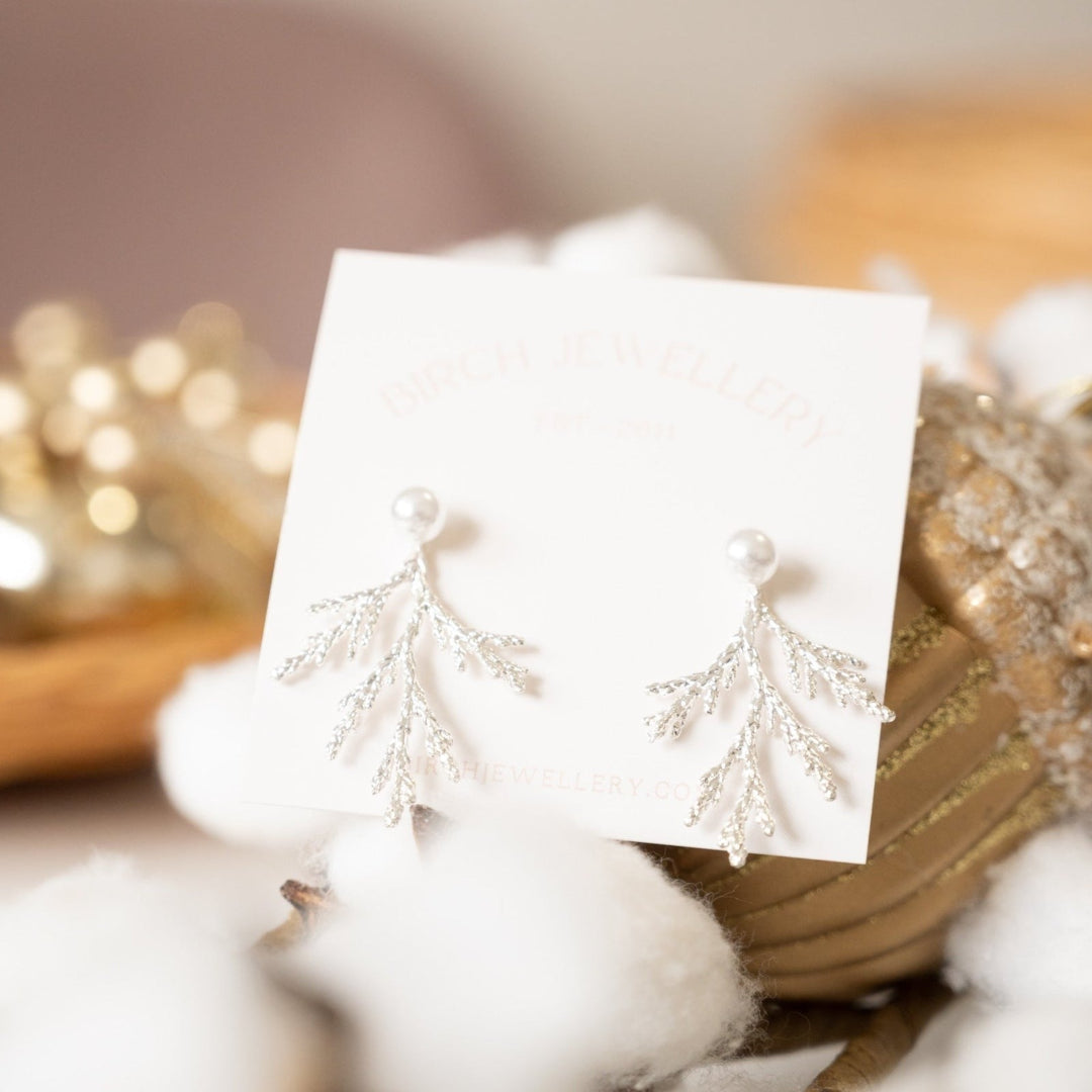 Silver earrings on a white card with a blurred decorative background