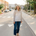 Brodie, one of the co-owners of Blondie Apparel standing on a street corner wearing a light-colored sweater and blue jeans.