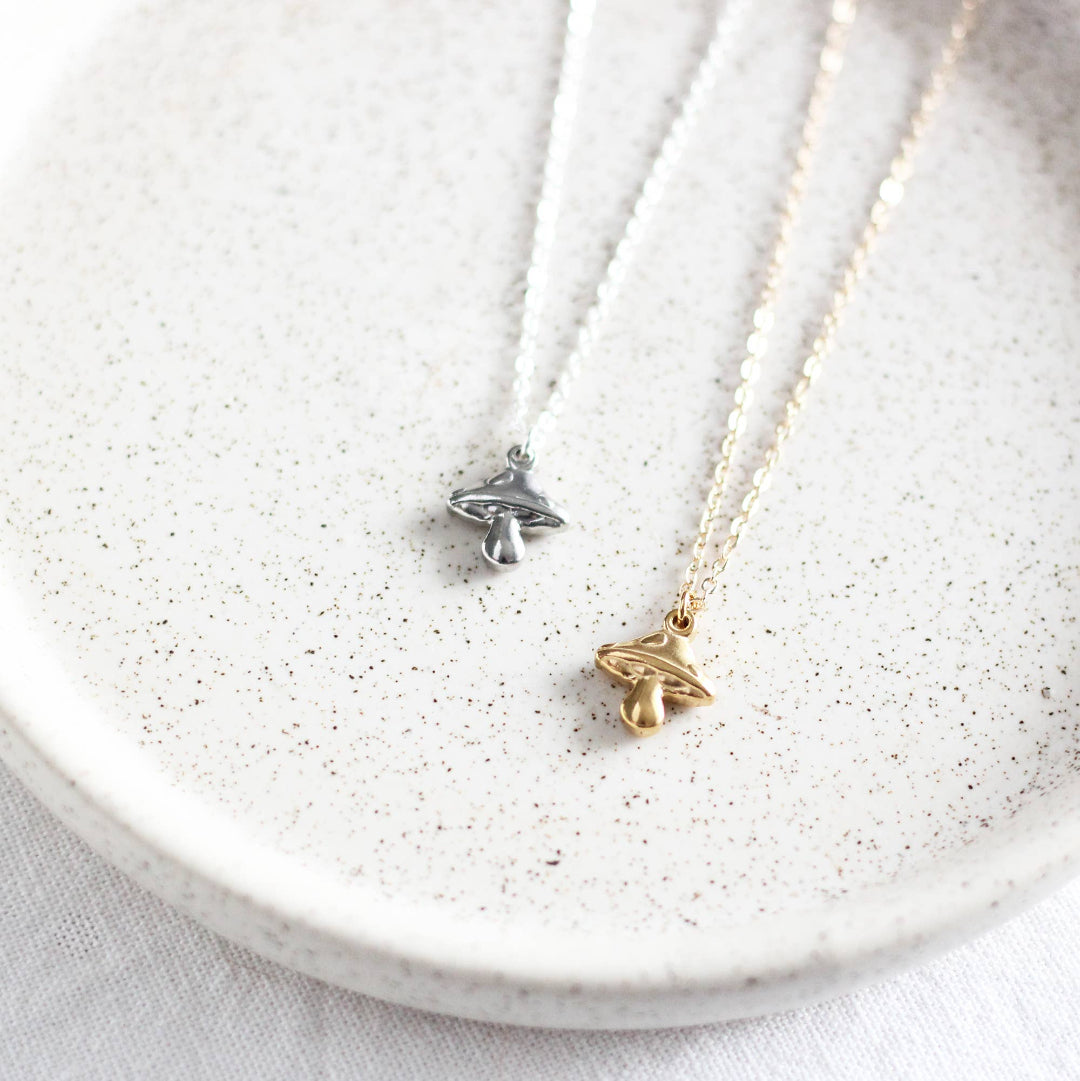 Two necklaces with butterfly pendants on a white speckled plate.