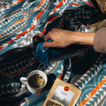 The Nibi Reversible Blanket by Mini Tipi, featuring bold Indigenous-inspired geometric patterns in teal, red, brown, and white, being used as a picnic blanket. This reversible and stylish blanket is available in Ottawa, Ontario, Canada.