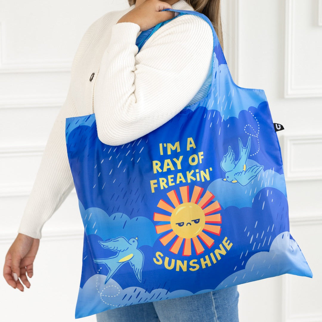 Woman holding a blue tote bag with a sun and cloud design, featuring text.