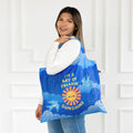 Person holding a blue tote bag with a sun design and text against a white door background