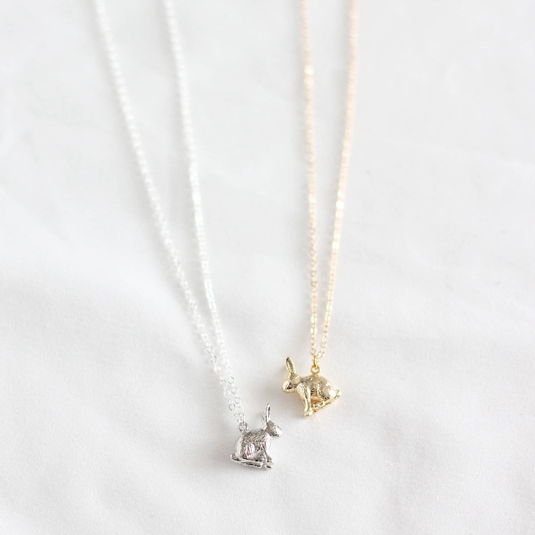 Two gold and silver cat-shaped pendants on thin chains against a white background.