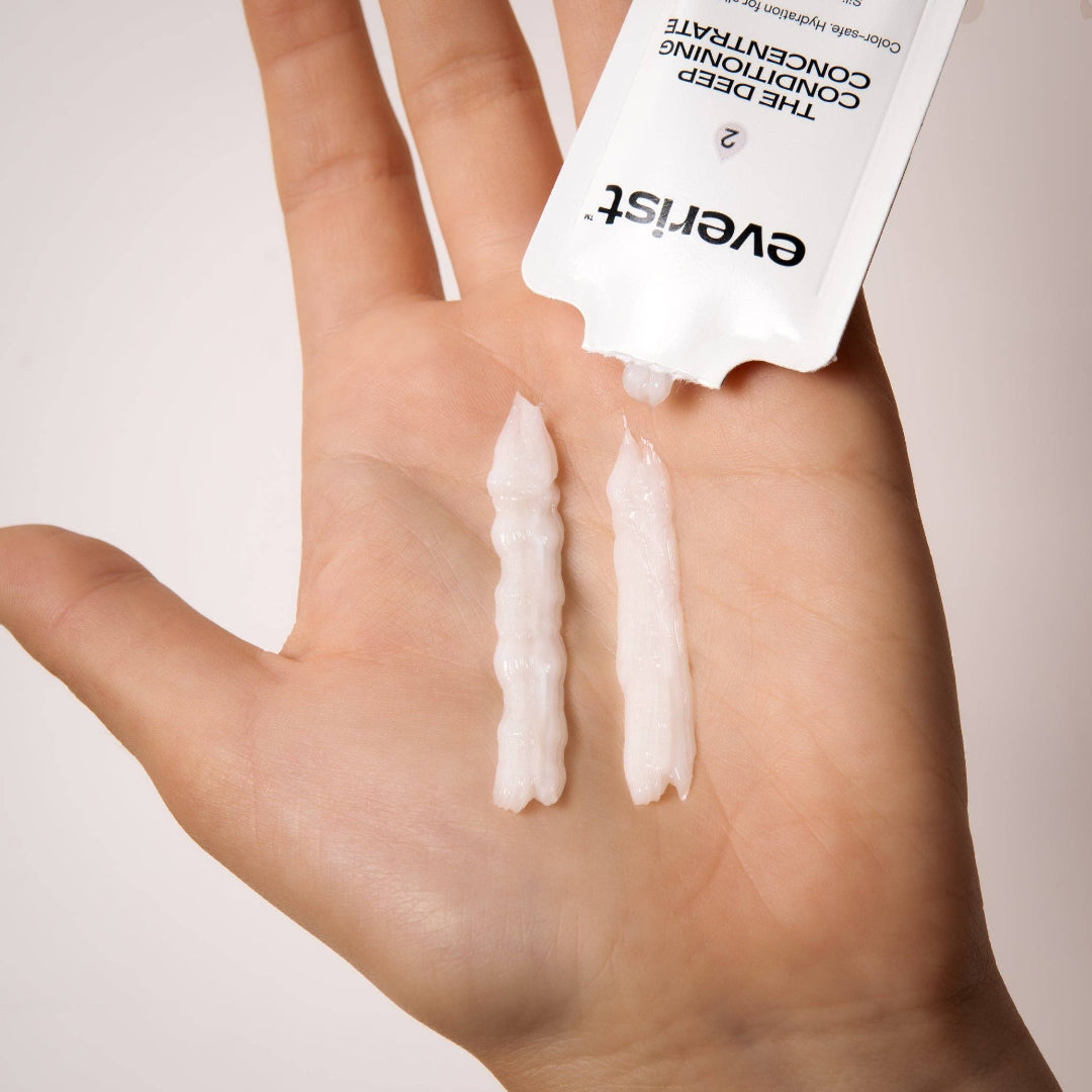 Hand holding a small amount of cream with a visible brand label on a neutral background