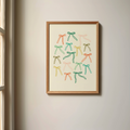 Colourful Bows Art Print in a wood frame hanging on a wall next to a window.