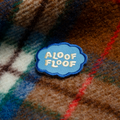Patch with 'Aloof Floof' text on a plaid fabric background
