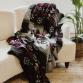 The Éclair Eco-Friendly Everyday Blanket by Mini Tipi, featuring bold Indigenous-inspired geometric patterns in black, grey, burgundy, turquoise, and yellow, draped on a sofa. This sustainable and stylish blanket is available in Ottawa, Ontario, Canada.