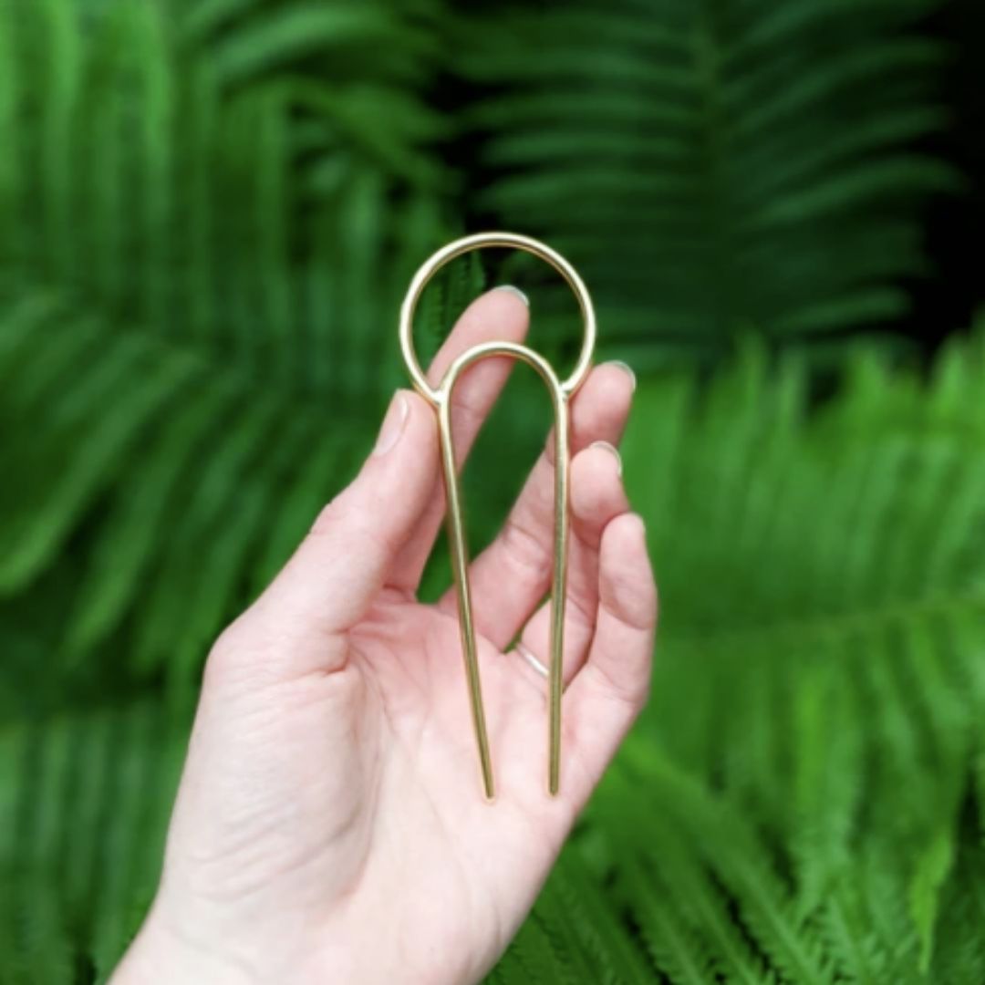 Hand holding brass crescent hair fork 